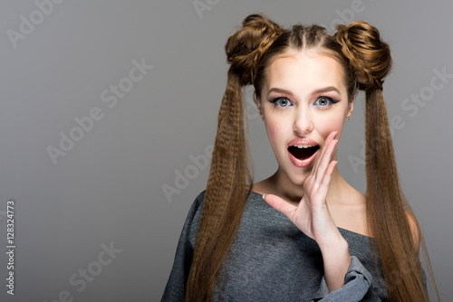 Fotografie, Obraz Portrait of a beautiful young girl with two ponytails, open mouth and hand express surprise, shock, gossip