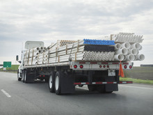 Rear And Side View Of Flatbed Semi Hauling Cargo Of Construction Pipes. Horizontal.