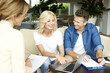 © sepy - Investment advisor and her clients. Shot of a happy middle aged couple consulting with real estate agent businesswoman in their home while sitting on couch.