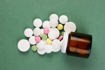 Wall Mural - Scattered pills and a jar on a green background