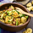 Baked cheese tortellini or belly button pasta with zucchini, bacon and thyme in wooden bowl, photographed with natural light (Selective Focus, Focus in the middle of the dish)