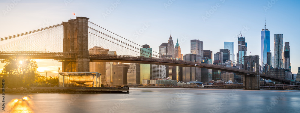 The panorama view of Brooklyn Bridge with Lower Manhattan in the background, lit by sunset - obrazy, fototapety, plakaty 