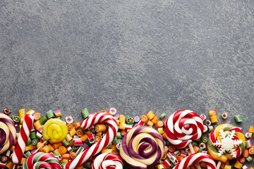 Wall Mural - Colorful lollipops, candy canes and sweet candies mix on stone textured background