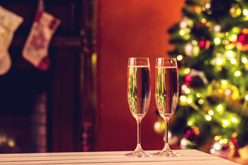 Beautiful two glasses of champagne standing on the table in the background of a blurred room with a decorated Christmas tree and fireplace. Soft focus. Shallow DOF