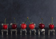 Row of red delicious cherries placed on tiny vintage silver chairs on dark background with copy space