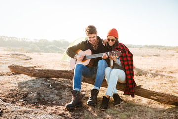 Poster - Couple having fun outdoors with guitar while sitting at campsite