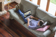 © GENETTICA - Young man lying comfortably on the sofa while using laptop with video steaming website on the screen. View from top. All screen graphics are made up.