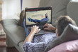 © GENETTICA - Young man lying comfortably on the sofa while watching video streaming on his laptop. All screen graphics are made up.
