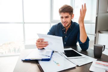 Sad man gesturing with hand and looking at documents