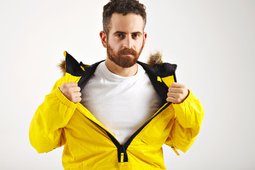 Wall Mural - Sexy bearded young man showing plain white t-shirt under his bright yellow snowboarding jacket isolated on white