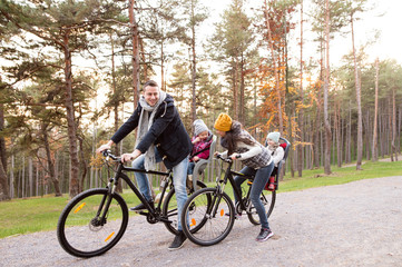 Wall Mural - Young family in warm clothes cycling in autumn park