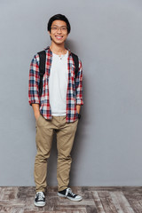 Poster - Smiling asian man with backpack standing holding hands in pockets