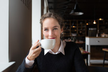 Smiling Young Woman Drinking Coffee While Sitting In The Cafe