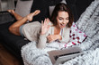 © Drobot Dean - Smiling girl waving hand while lying on couch with laptop