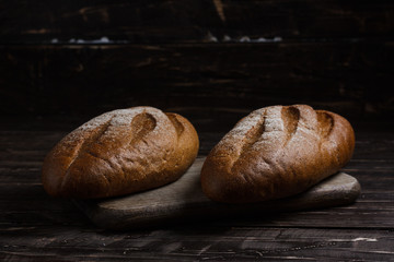 Two black bread with flour on a wooden background. Advertising bread. Leaning flour.