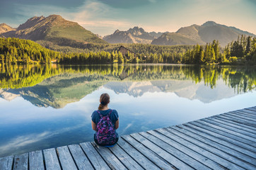 Wall Mural - alone young girl sitting and resting on the wooden path near by beautiful blue lake and clear big mo