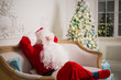 © romankosolapov - Santa Claus relaxing on sofa against christmas tree at home