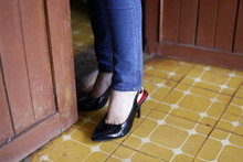 Young Fashionable Girl With Long Legs Wearing Black Shoes On Platform. Stand By The Red Door