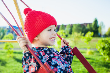 Expressive little girl on swing, smiling happily with all her teeth, having fun on playground, closeup portrait. Happy childhood concept