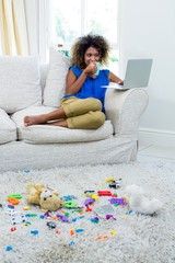 Poster - Young woman using laptop while having coffee in living room