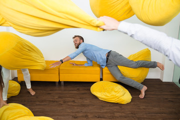 Wall Mural - Cheerful young man on couch among flying beanbags