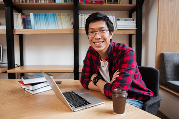 Wall Mural - Asian man using laptop at the library and drinking coffee