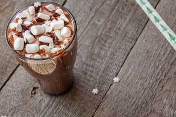 Sticker - Winter hot cocoa with marshmallows, chocolate syrup, sugar snowflakes in a tall glass on a wooden background.