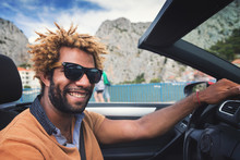Young Happy Black Man With Dread Locks Wearing Sunglasses Sitting In The Convertible Car. Vintage Film Effect Applied.