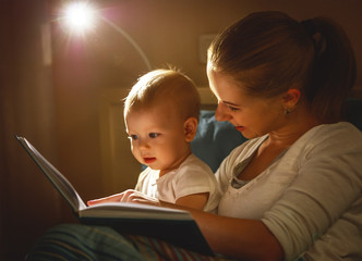 mother and baby son reading a book in bed