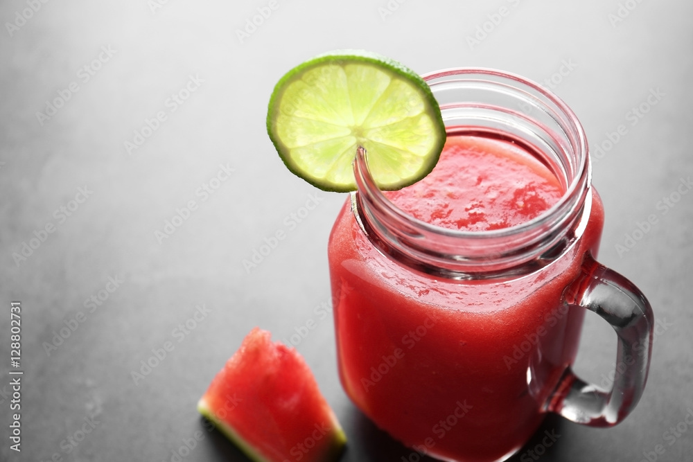 Jug with smoothie and watermelon slice on grey table