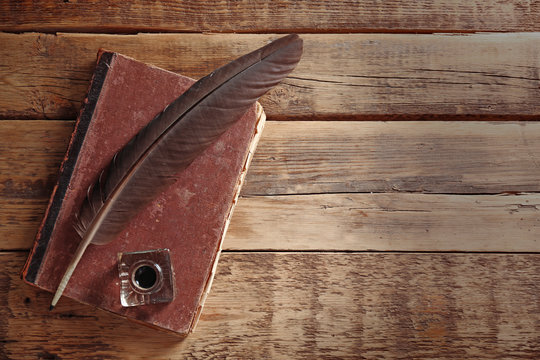 Feather pen with inkwell and old book on wooden table closeup