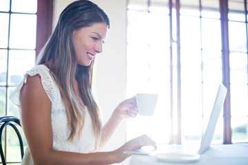 Poster - Smiling woman using a laptop while having a coffee