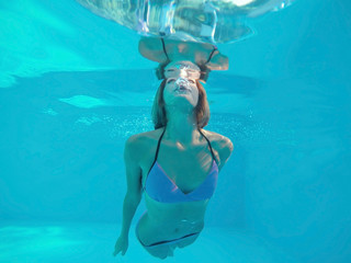 Beautiful young woman swimming under water in pool