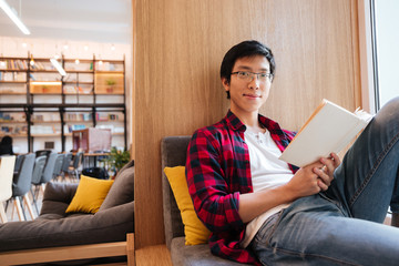 Canvas Print - Asian student reading book in university library sitting on sofa