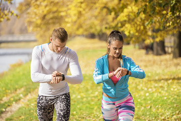 Beautiful young couple preparing their watches for run in the park. Autumn environment.