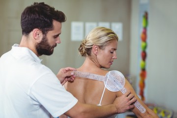 Wall Mural - Male therapist measuring female patient back with goniometer