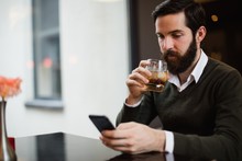 Man Having Glass Of Drink While Using Mobile Phone