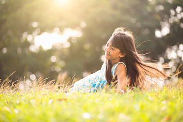 cute little asian girl laying in the grass on a sunny summer day, outdoor portrait