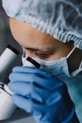 Wall Mural - from above view of young scientist in work uniform looking at microscope.