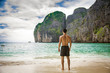 © theartofphoto - Full body shot from the back of a handsome young man standing on a beach in Phuket Island, Thailand, shirtless wearing boxer shorts, showing muscular fit body