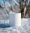 white mug with a hot drink in winter on snow on the nature table
