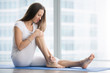 © fizkes - Unhappy young woman sitting on the mat, grabbing an ankle, unable to start yoga work out because of sport injury, feeling pain. Beginner doing wrong exercise without coacher