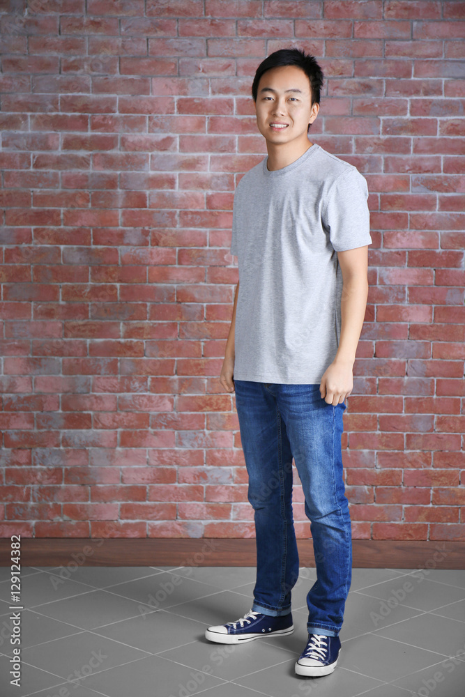 Asian man in blank grey t-shirt standing against brick wall