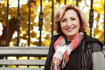 Gorgeous middle aged woman sitting on bench in autumn park