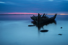 Old Broken Boat Wreck On The Shore, A Frozen Sea And Beautiful Blue Sunset Background. Estonia, Europe.