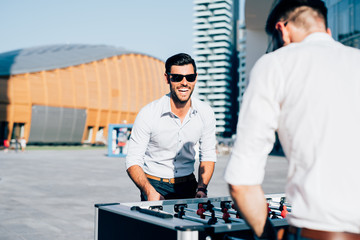 Knee figure of two modern bearded businessman playing table football during a break, focus on the blonde one - having fun, break, playing concept