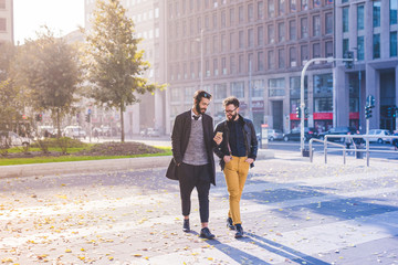 two young bearded blonde and black hair modern businessman, walking in the city using smart phone - 