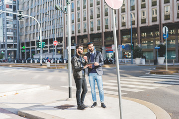 two young bearded modern businessman using tablet handhold outdoor in the city, discussing - technol