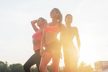 Group of fit young sportswomen standing in athletics stadium and posing.