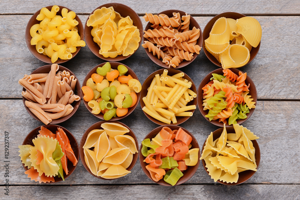 Different kinds of pasta in bowls on wooden background